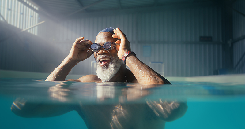 Senior, black man and goggles in swimming pool for fitness, physical therapy and physiotherapy for arthritis management. Male person, indoor aquatic center and hydrotherapy for mobility strength.